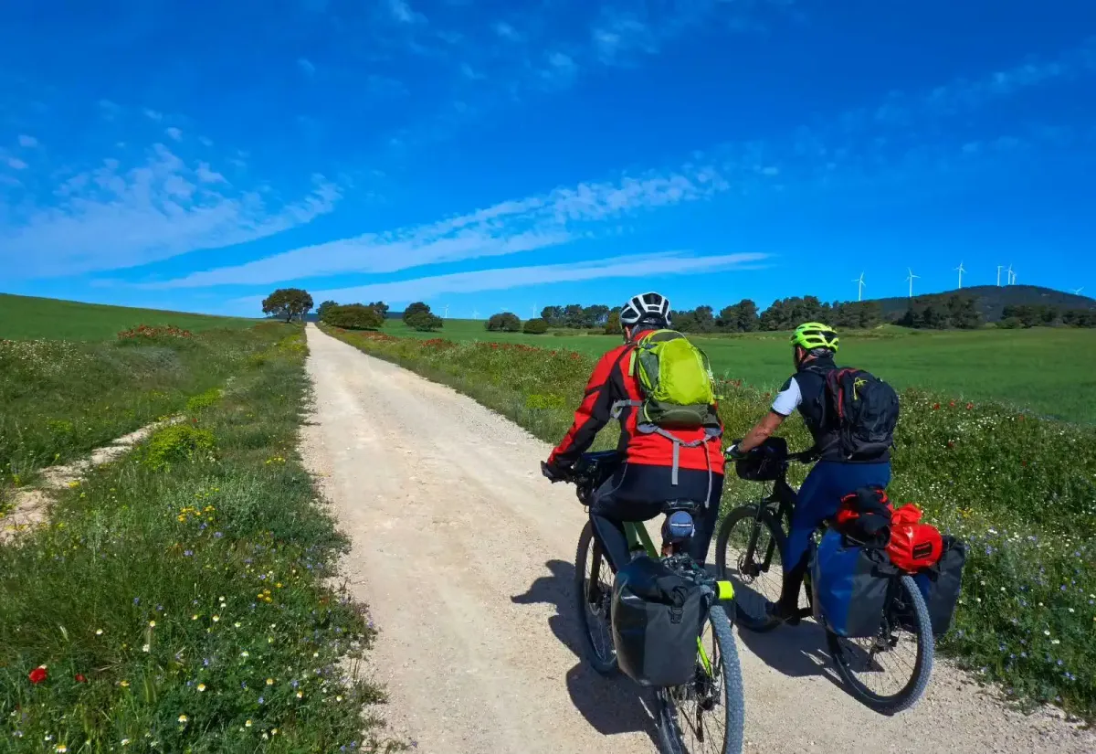 Dos ciclistas con alforjas pedalean por un camino de tierra rural