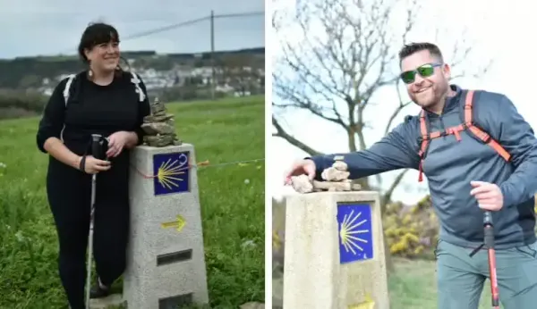 Dos personas posan junto a mojones con la concha y la flecha amarilla del Camino de Santiago.