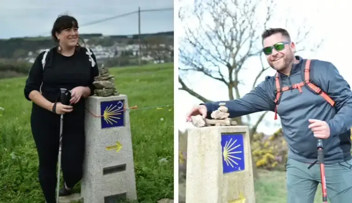Dos personas posan junto a mojones con la concha y la flecha amarilla del Camino de Santiago.