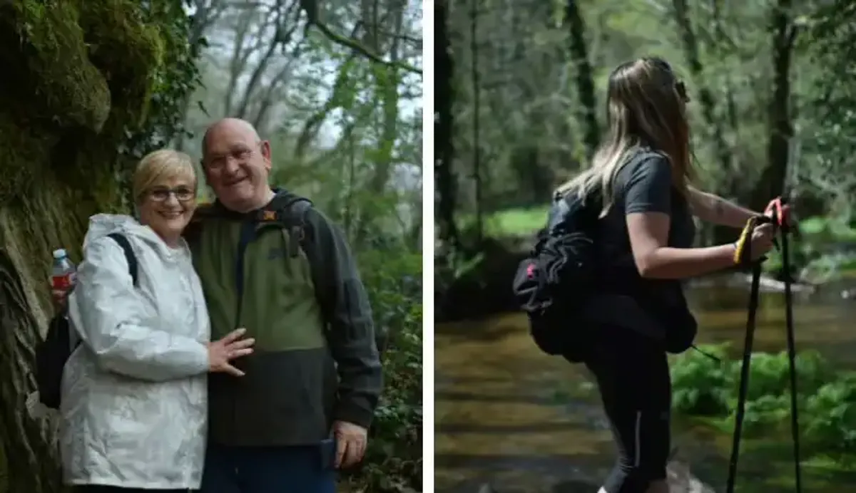 Un grupo de peregrinos camina por un sendero arbolado durante el Camino de Santiago, mostrando una pareja sonriente y una mujer usando bastones.