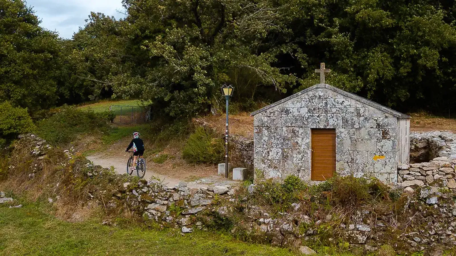 Peregrino en bici cruzando junto a la Capilla de Castro en Muxía