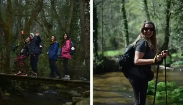 Senderistas sonriendo cruzan un puente sobre un río. Con mochilas y bastones, disfrutan de su caminata grupal por un tramo boscoso del Camino de Santiago.