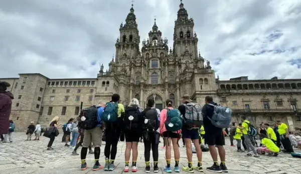Un grupo de peregrinos con mochilas frente a la fachada de la Catedral de Santiago de Compostela tras completar el Camino de Santiago.